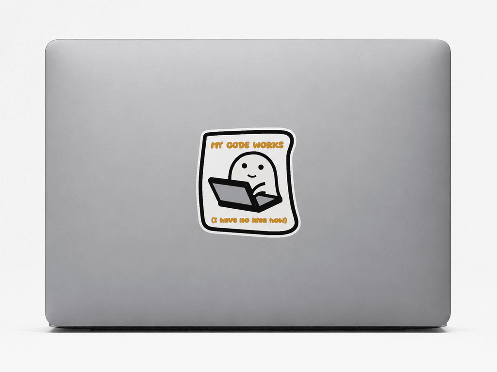 A square vinyl sticker with a cartoon ghost sitting at a laptop, displayed on the back of a silver laptop. The sticker features the text 'MY CODE WORKS' in orange at the top and 'IT HATS NOT HATS' in orange at the bottom.