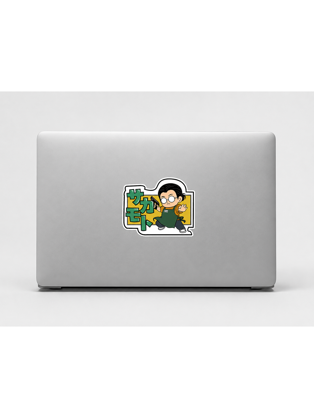 A silver laptop closed and viewed from the back, with taro sakamoto from the anime 'sakamoto days' on the center. The sticker features a character in green and yellow with Japanese text.